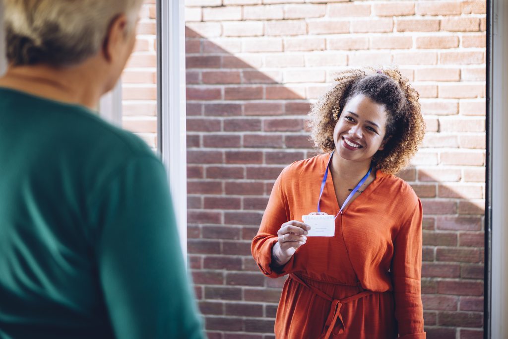 Healthcare worker showing her badge at the front door of a senior womans home.
